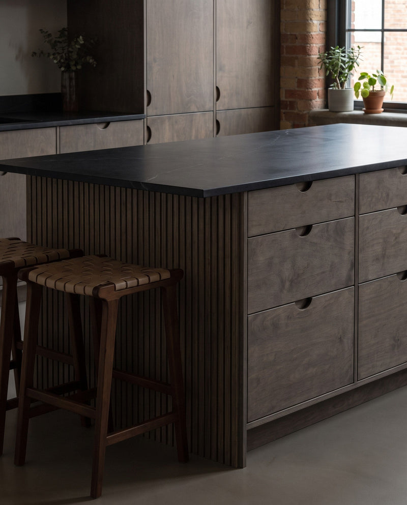 Concept: a kitchen island in dark-stained birch plywood with half-moon cut-in pulls, a reeded end panel and a dark stone worktop