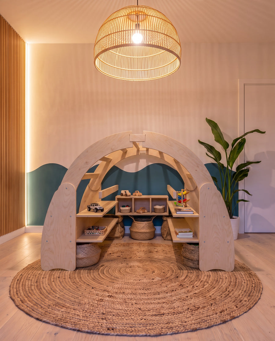 Render: the Ply Arch play den in Natural birch plywood, with built-in shelves and cubbies, on a jute rug